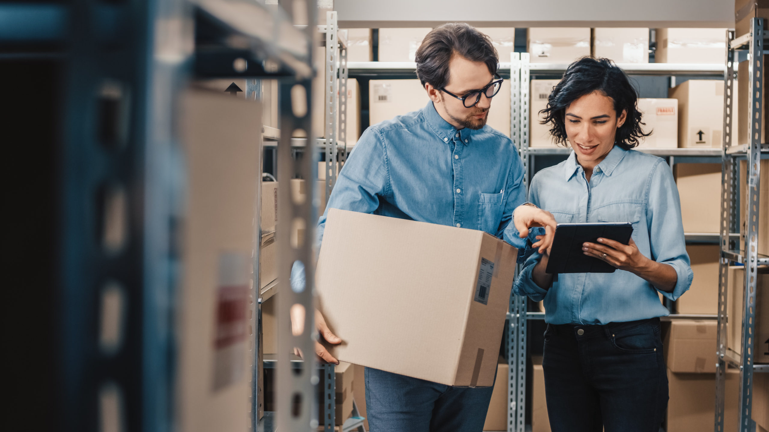 Female Inventory Manager Shows Digital Tablet Information to a Worker Holding Cardboard Box, They Talk and Do Work. In the Background Stock of Parcels with Products Ready for Shipment. PG征途国际官方网站图片